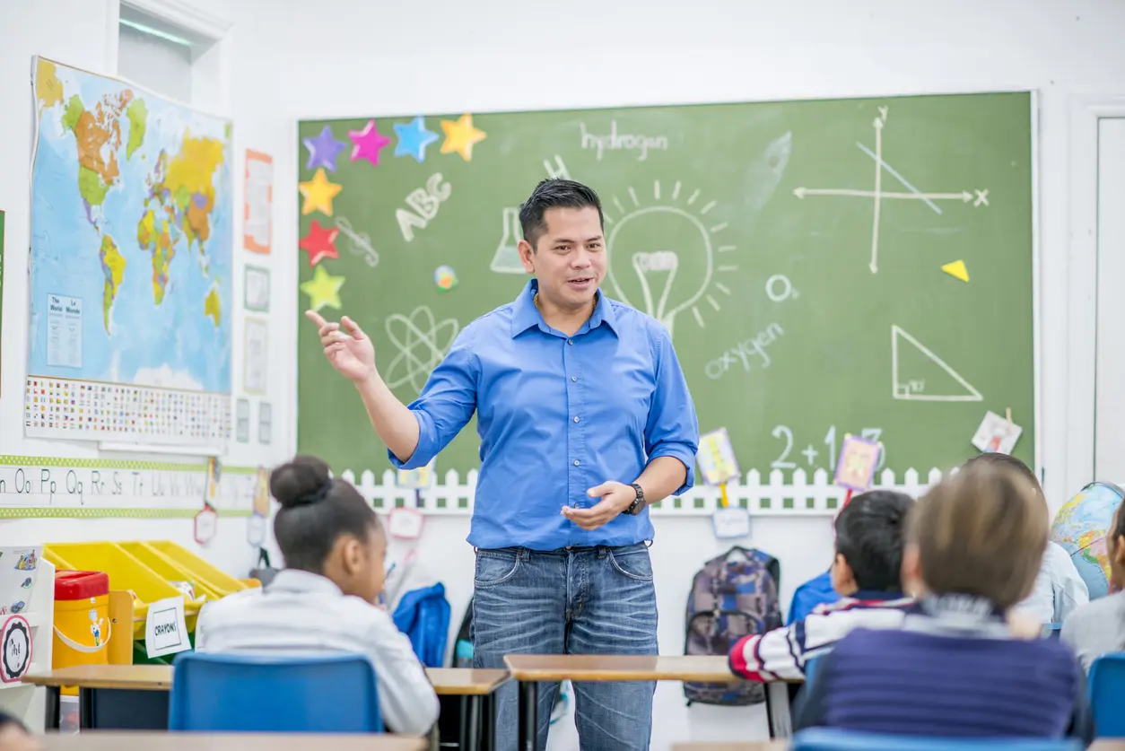 Elementary school teacher leading a lesson in front of a classroom with students listening